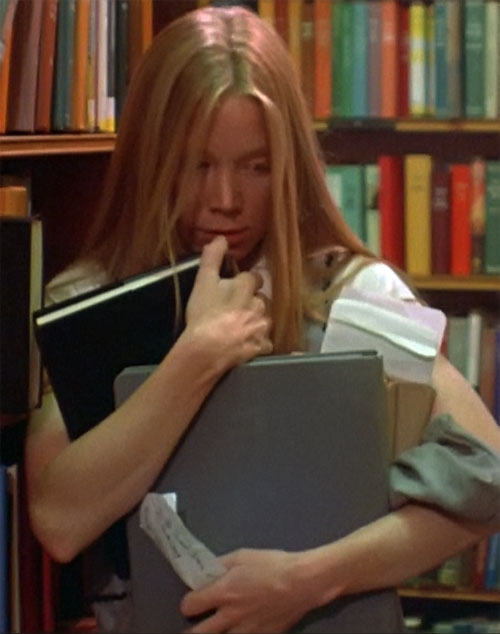 Carrie in the library holding books to cover her face.